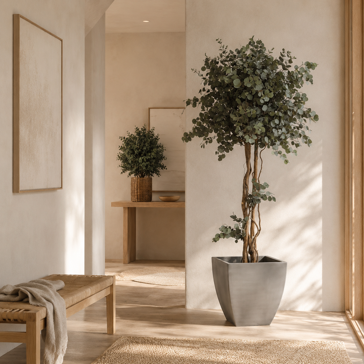 Konstgjort eukalyptusträd i grå kruka och mindre krukväxt i en ljus, minimalistisk hallmiljö